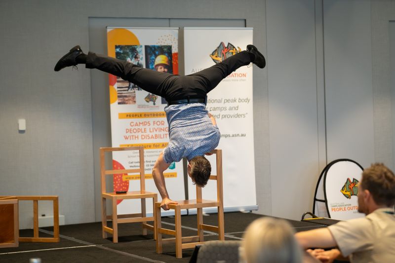 Dan Aubin performing a handstand on a chair to ACA delegates